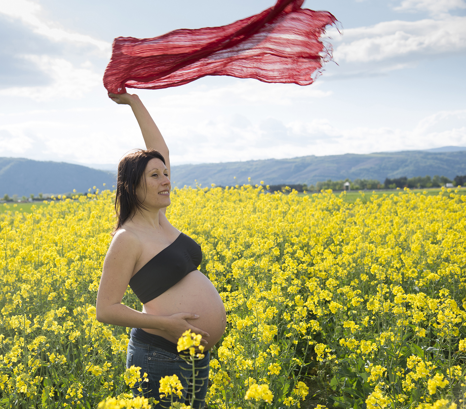 femme enceinte dans des champs de colza avec un foulard rouge au vent