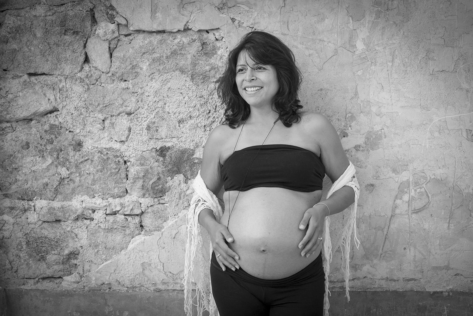 femme enceinte en noir et blanc devant un vieux mur en pierre